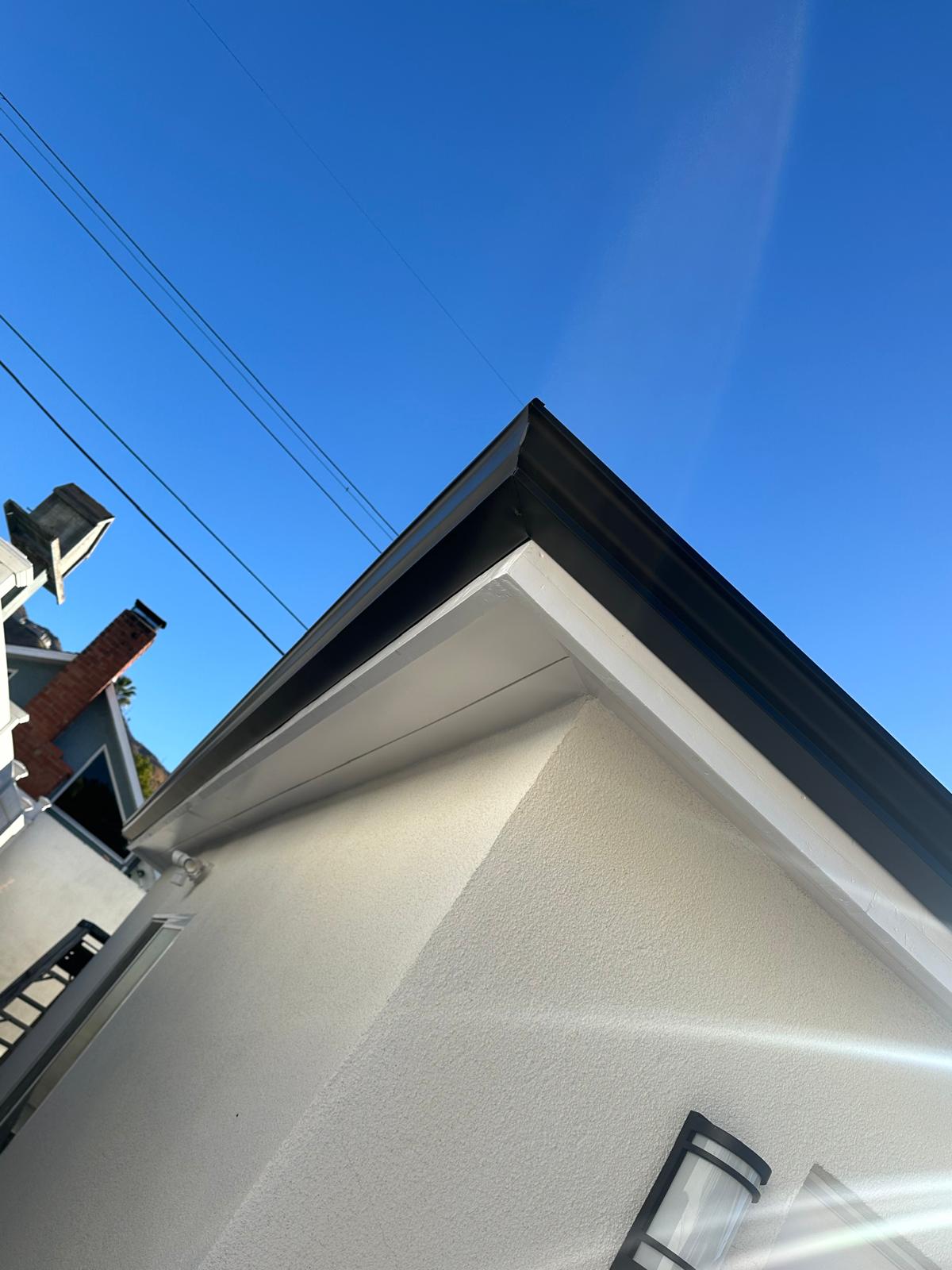 Black gutter corner detail against a clear blue sky